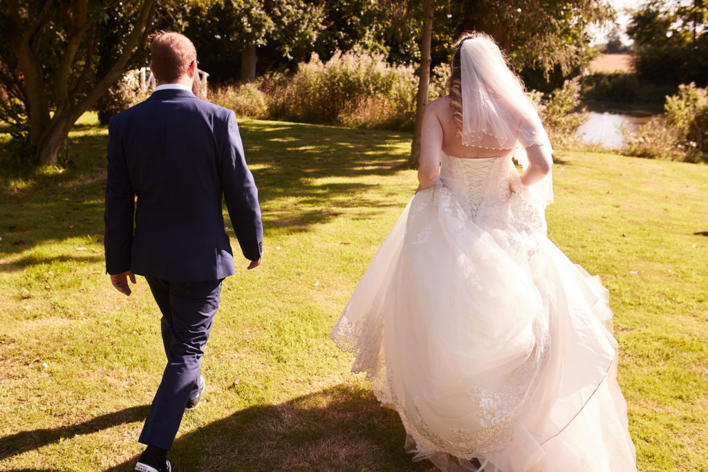 Bride and groom walking across the lawn at Villiers Barn, seen from behind