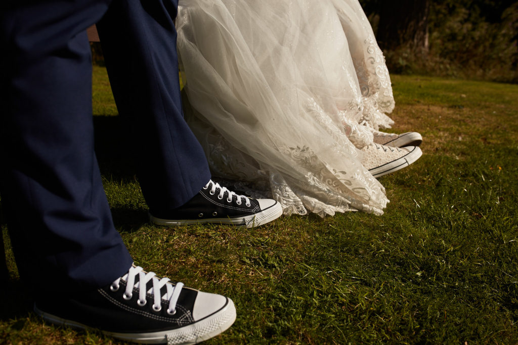Close-up of the groom's Converse trainers beside the hem of the bride's dress