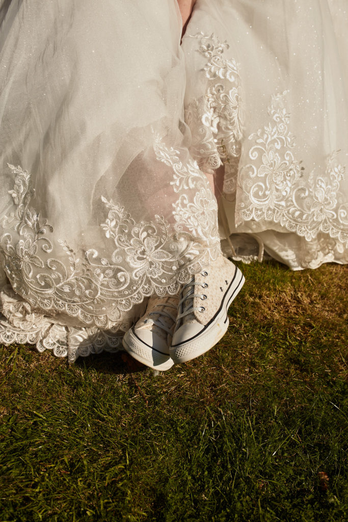 Bride's white Converse trainers showing beneath the lace hem of her wedding dress
