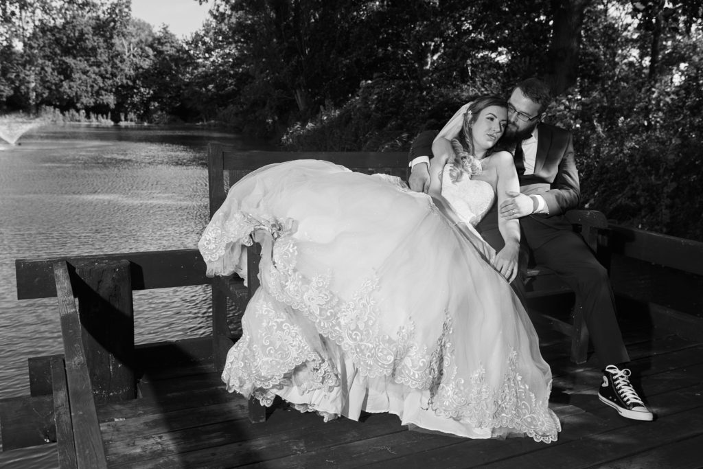 Black and white photo of the bride and groom on a bench beside the lake at Villiers Barn