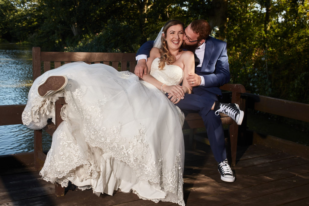 Bride and groom cuddling on a bench by the lake at Villiers Barn