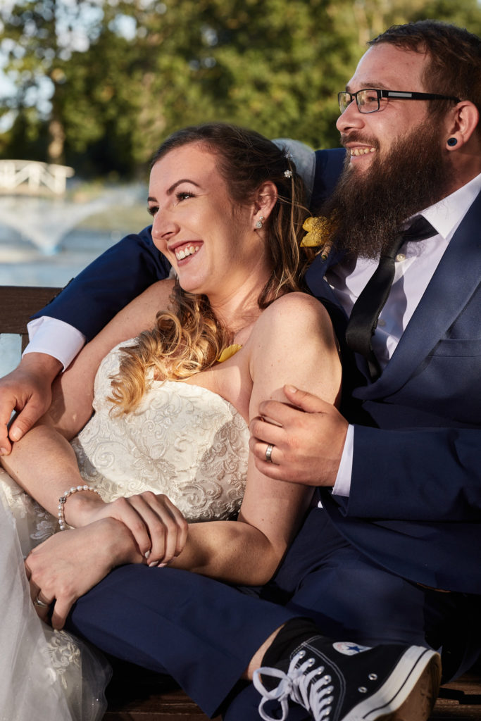 Bride laughing as the groom hugs her from behind beside the lake at Villiers Barn