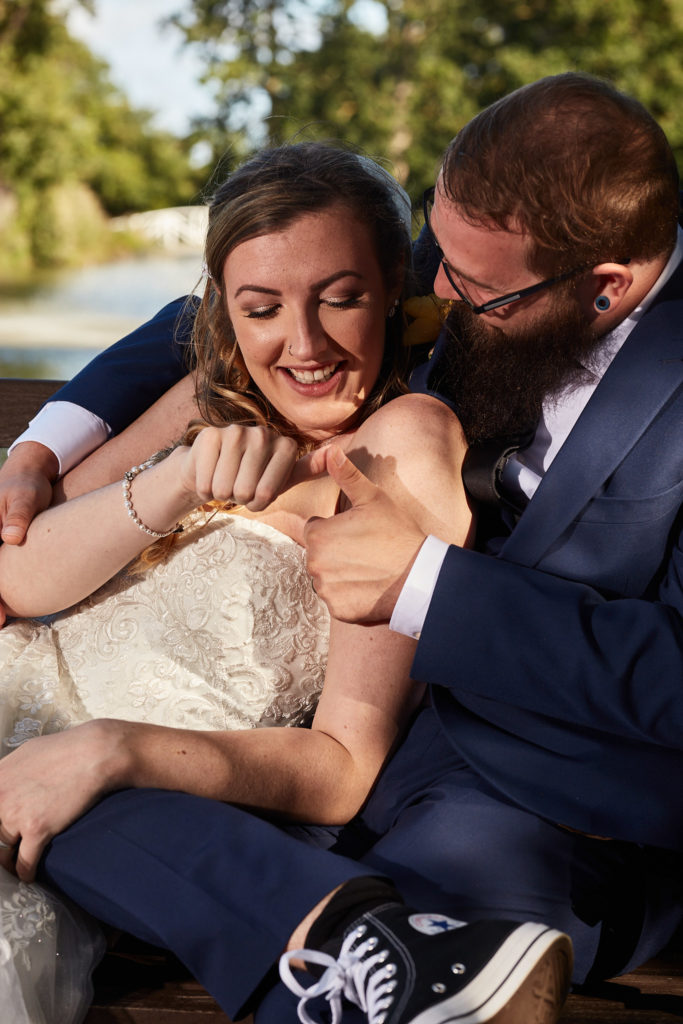 Bride and groom laughing together on a bench at Villiers Barn, the groom in Converse trainers