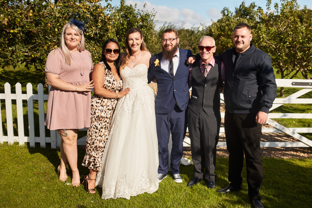 Bride and groom with four guests in front of a white fence