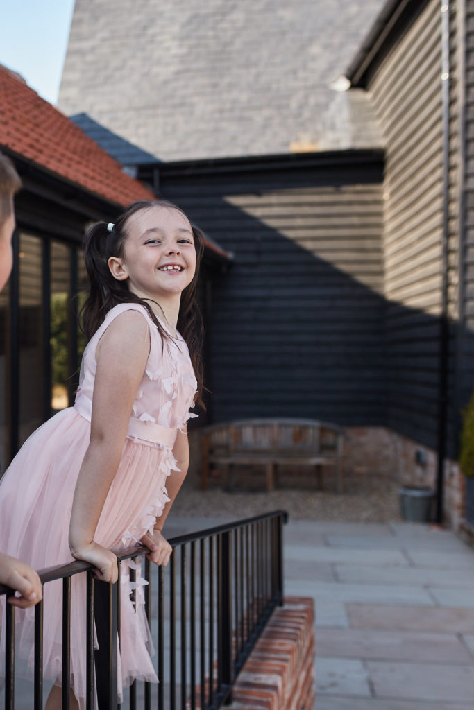 Young bridesmaid in a pink dress leaning on railings outside the black barn