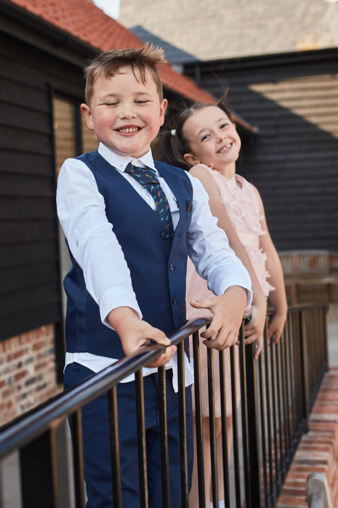 Page boy and young bridesmaid smiling on the railings outside Villiers Barn