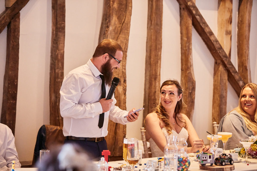 Groom giving his speech with a microphone as the bride listens
