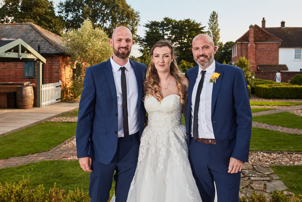Bride standing between two men in navy suits at Villiers Barn