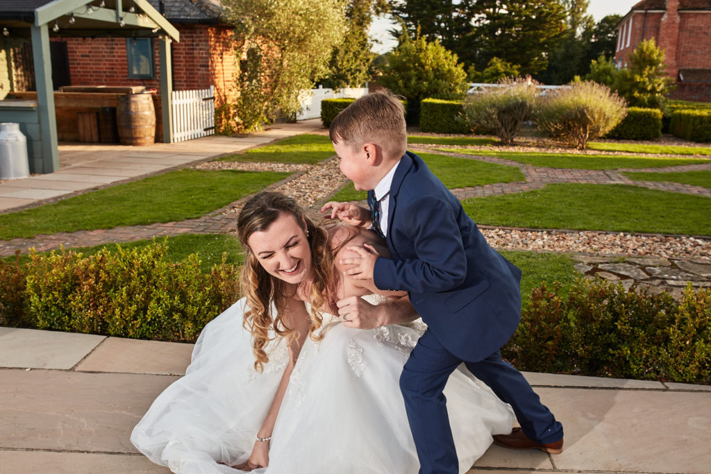 Page boy climbing on the laughing bride in the gardens