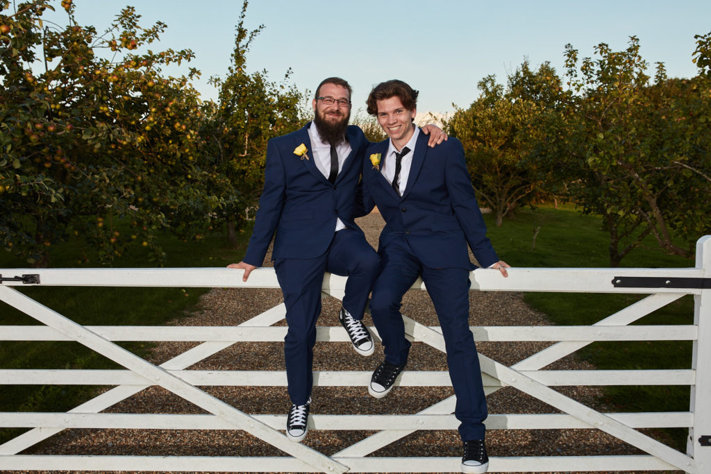 Groom and best man sitting on a white gate at Villiers Barn