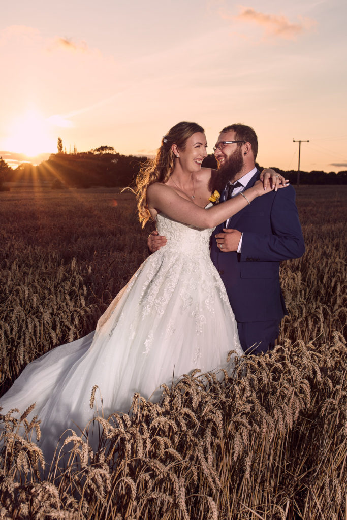 Bride and groom laughing in a wheat field at sunset near Villiers Barn, Clacton