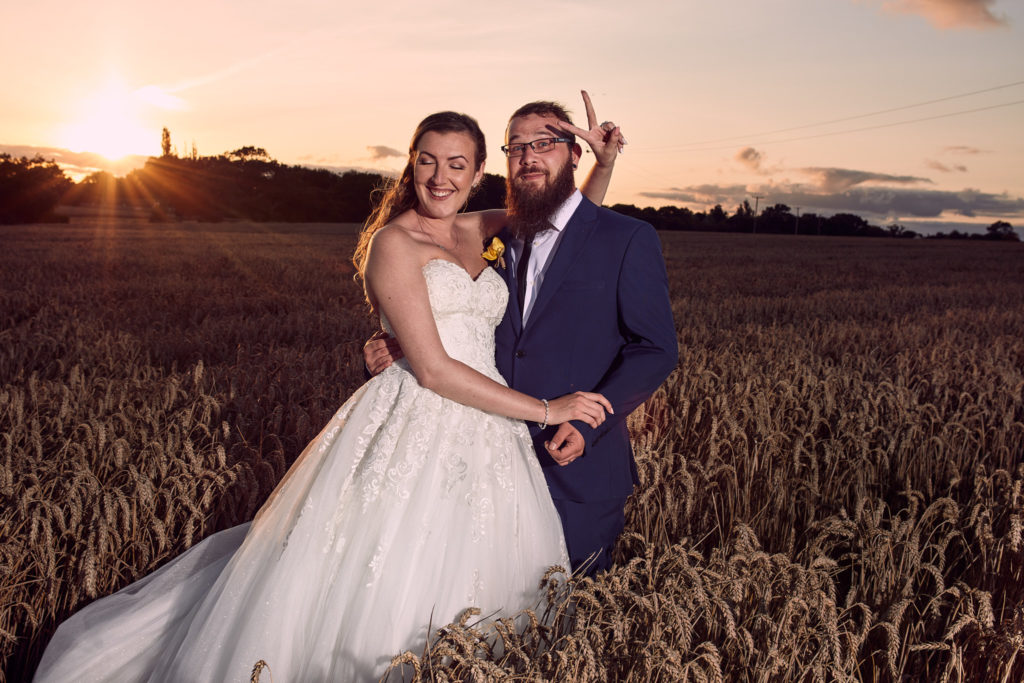 Bride and groom posing playfully in a wheat field at sunset at Villiers Barn