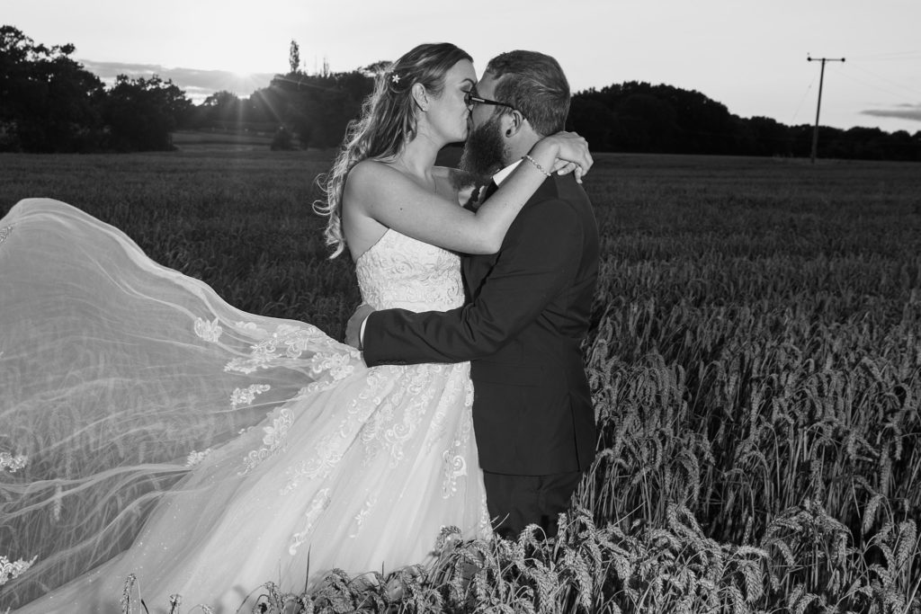 Black and white photo of the bride and groom kissing in a field at dusk at Villiers Barn