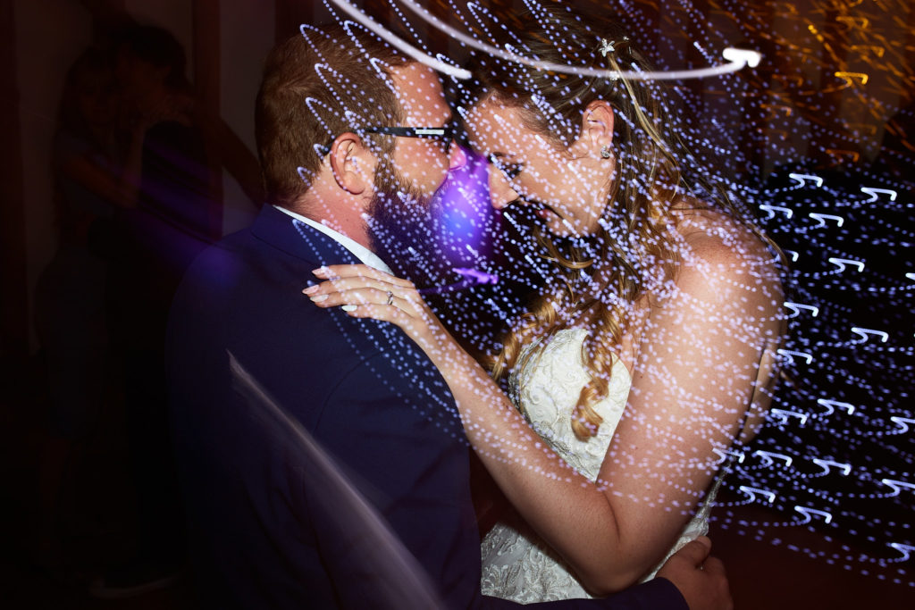 Bride and groom dancing close together among swirls of light