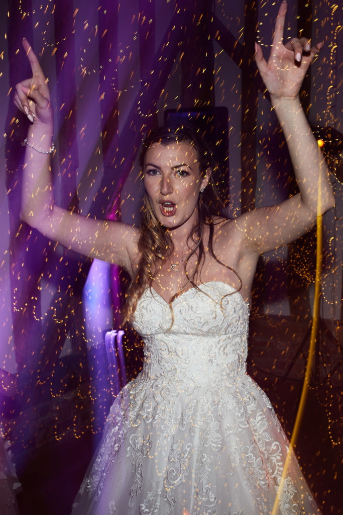 Bride dancing with her arms in the air under purple lights