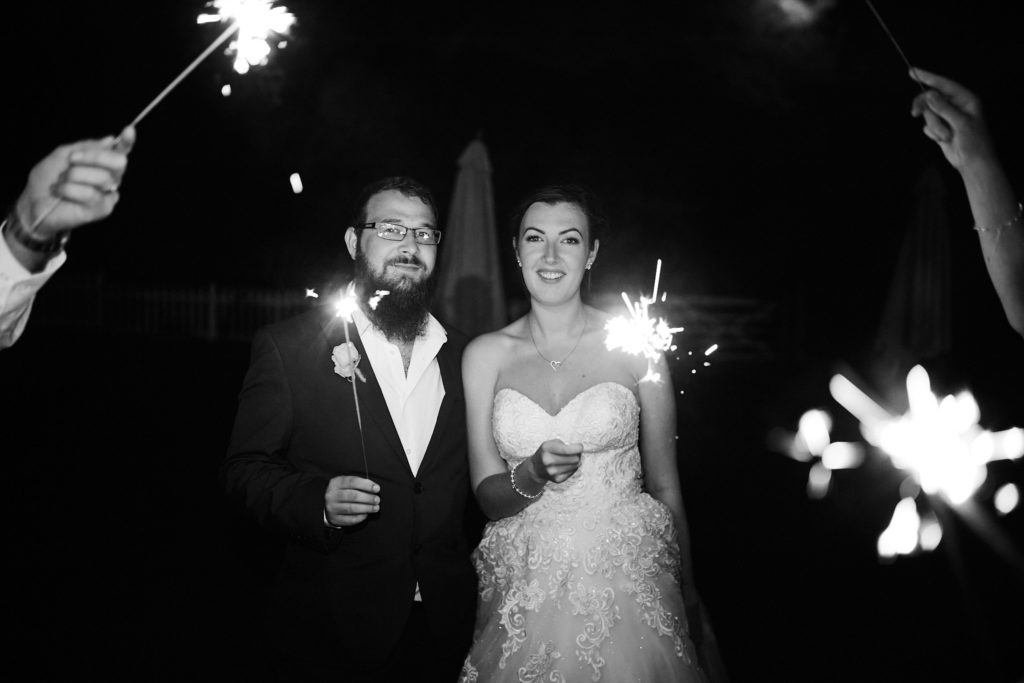Black and white photo of the bride and groom walking through a tunnel of sparklers