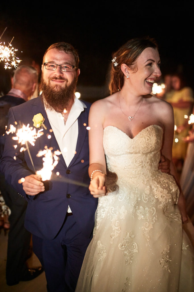 Bride and groom holding sparklers among their guests at night