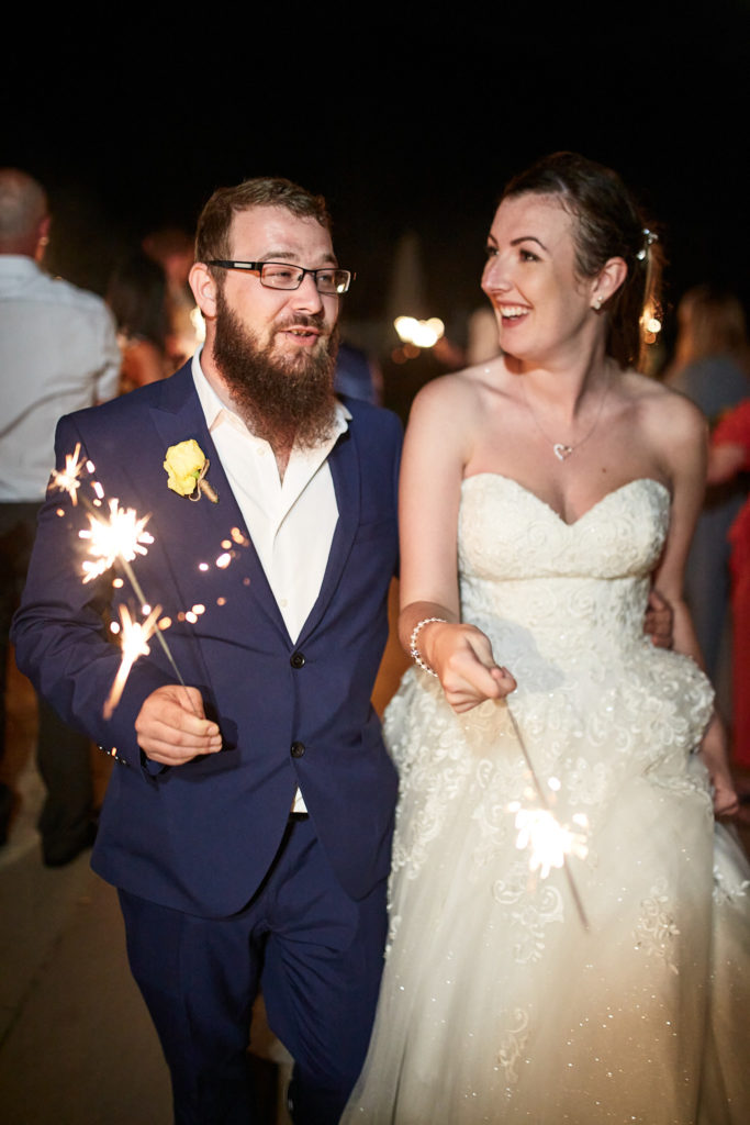 Bride and groom smiling at each other as they hold sparklers