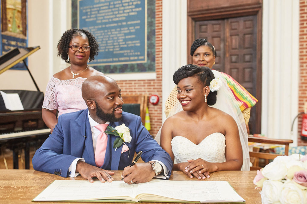 Bride and groom smiling as they sign the register with two witnesses behind them