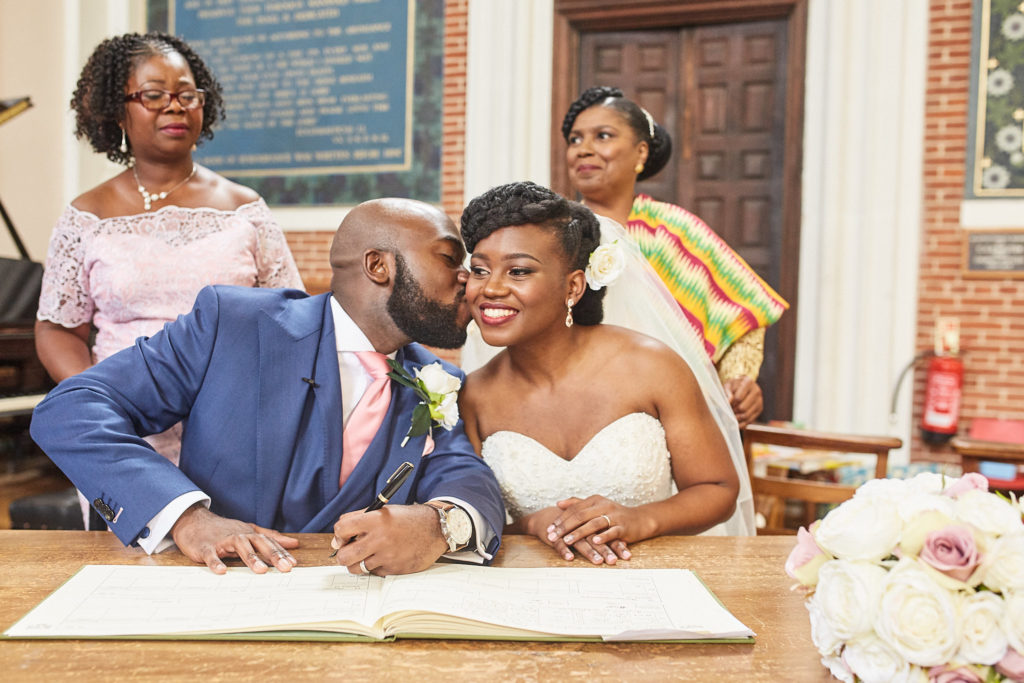 Groom kissing the bride's cheek as they sign the register