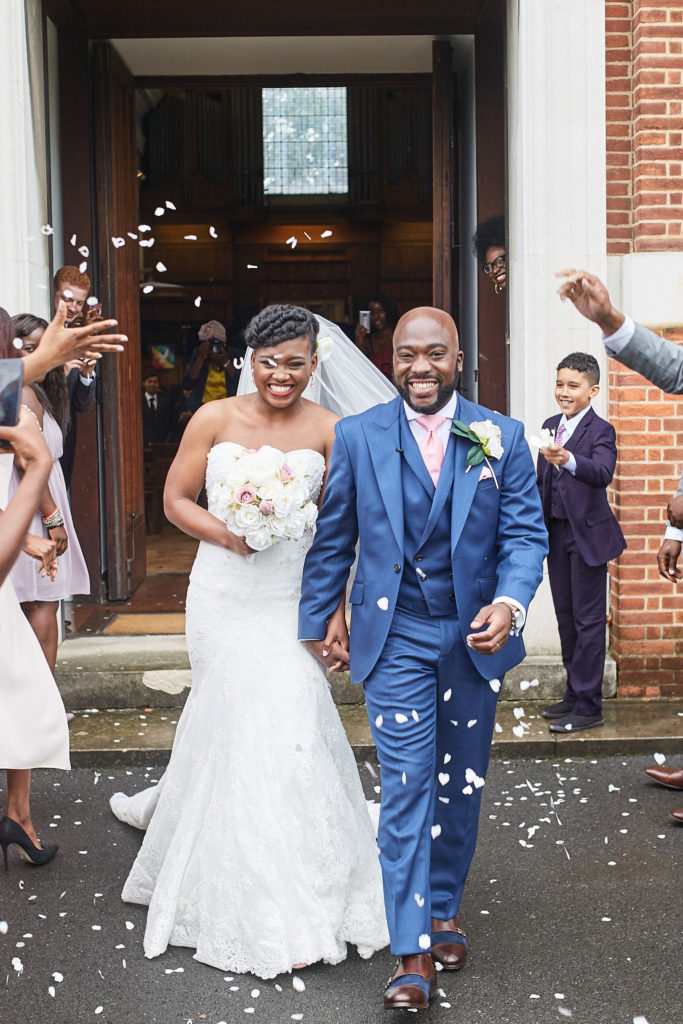 Bride and groom laughing under a shower of confetti outside the church