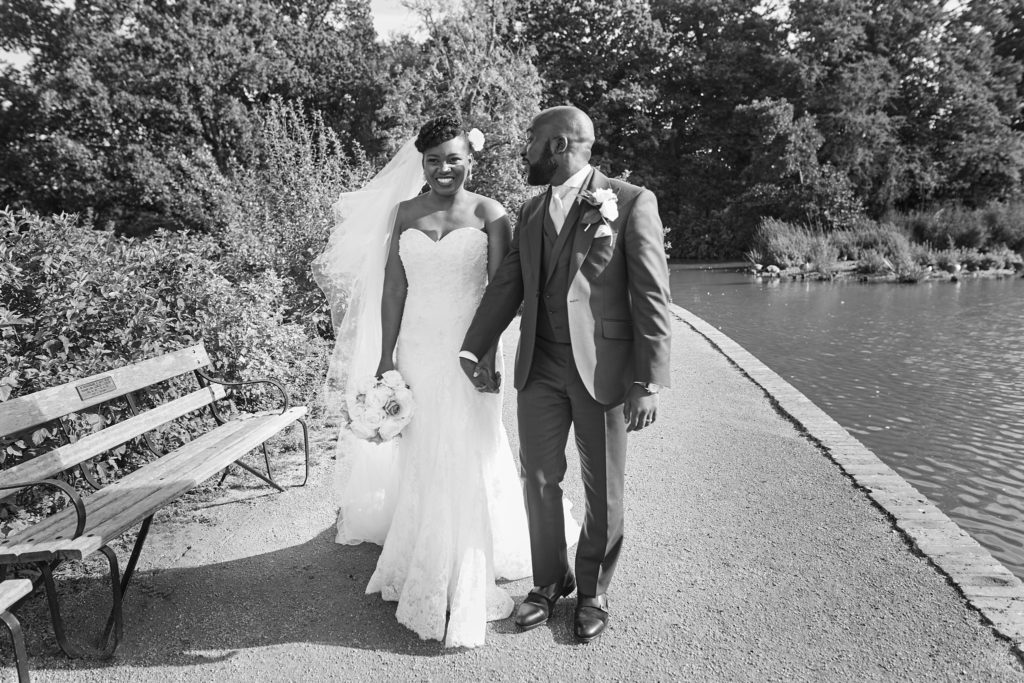 Black and white photo of the bride and groom walking along the lakeside path at Forty Hall