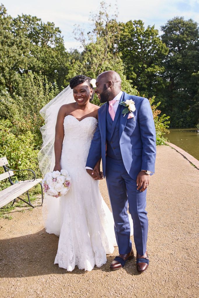 Bride and groom smiling arm in arm on the lakeside path at Forty Hall, north London