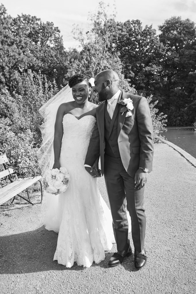 Black and white photo of the bride and groom laughing together by the lake at Forty Hall