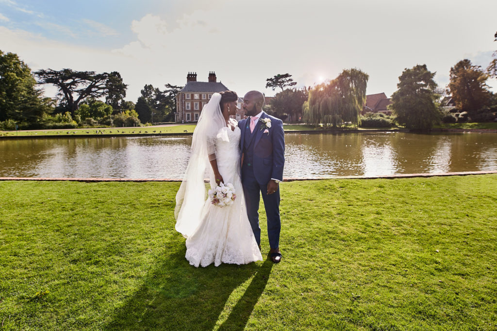 Bride and groom on the lawn beside the lake with Forty Hall behind them