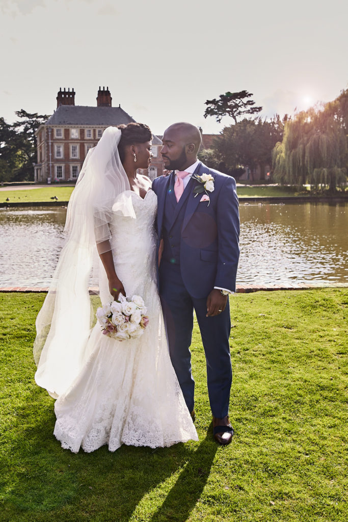 Bride and groom forehead to forehead on the lawn with Forty Hall across the lake