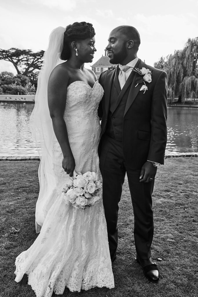 Black and white photo of the bride and groom smiling at each other by the lake at Forty Hall