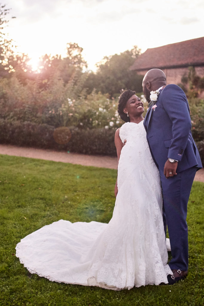 Bride laughing as the groom leans in close at sunset at Forty Hall, her dress train spread on the grass