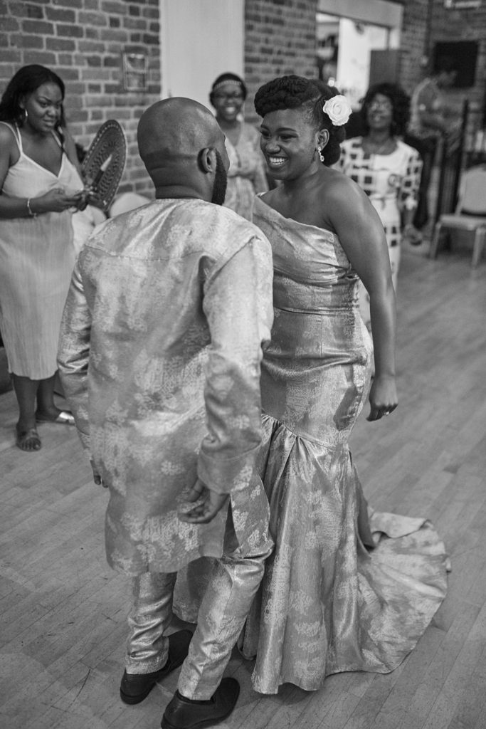 Black and white photo of the bride and groom dancing in traditional outfits among their guests