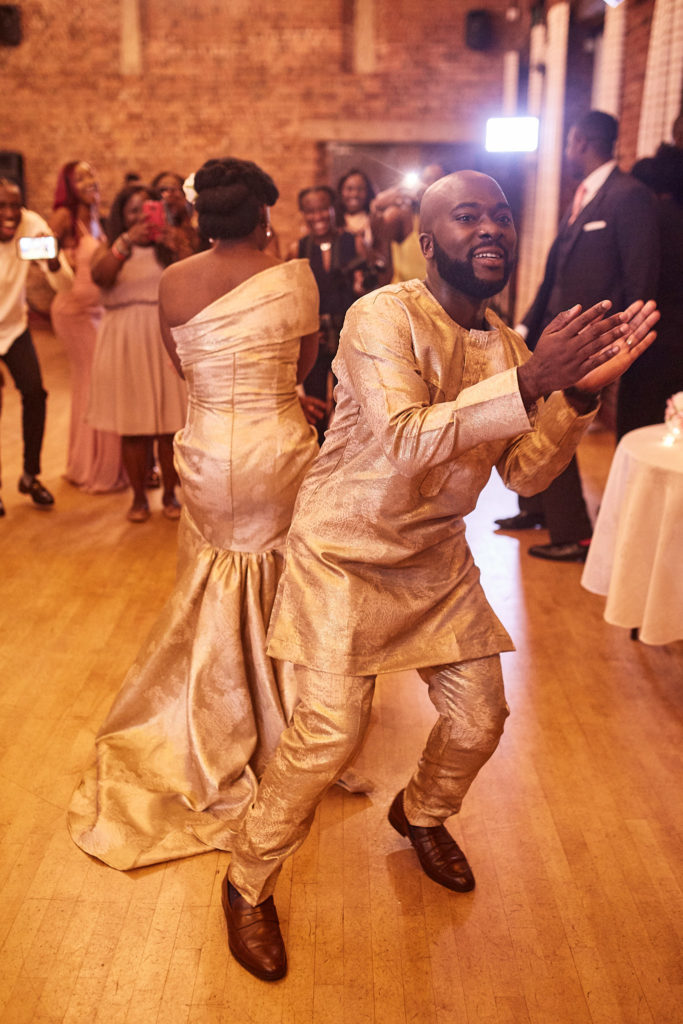 Bride and groom dancing in matching gold traditional outfits as guests cheer