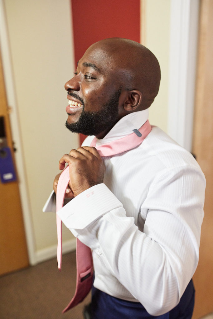 Groom laughing as he ties his pink tie