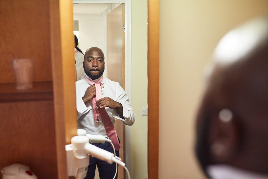 Groom tying his pink tie in a doorway