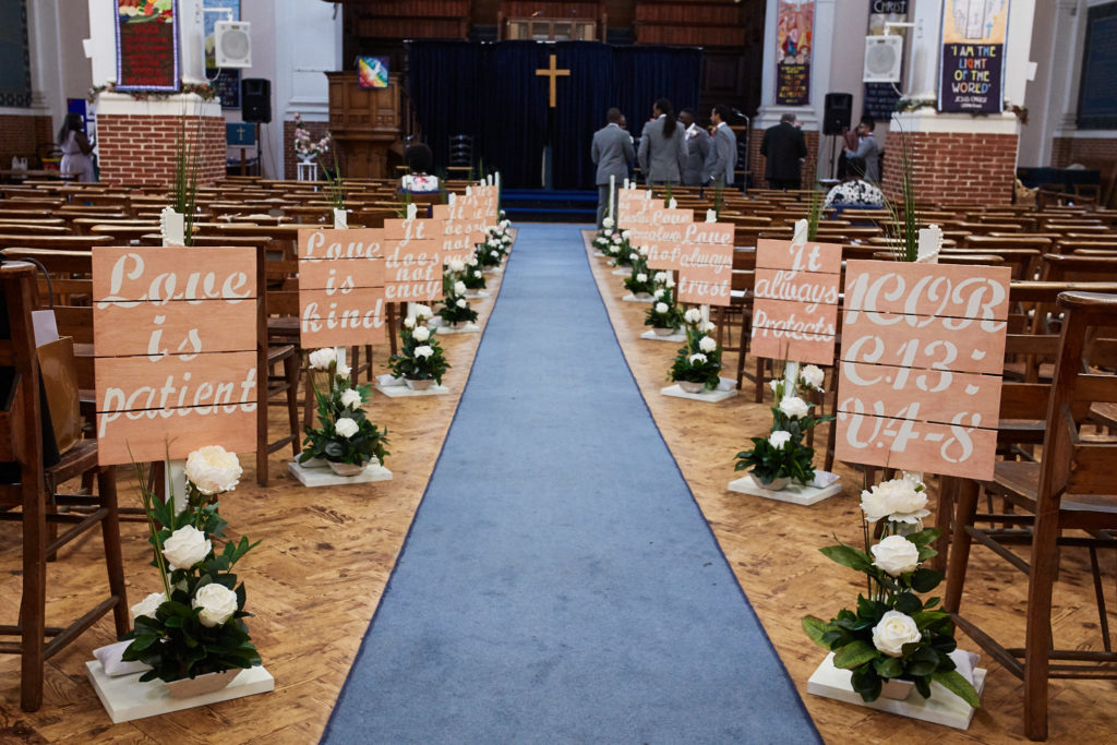 Church aisle with a blue carpet lined with flowers and wooden signs