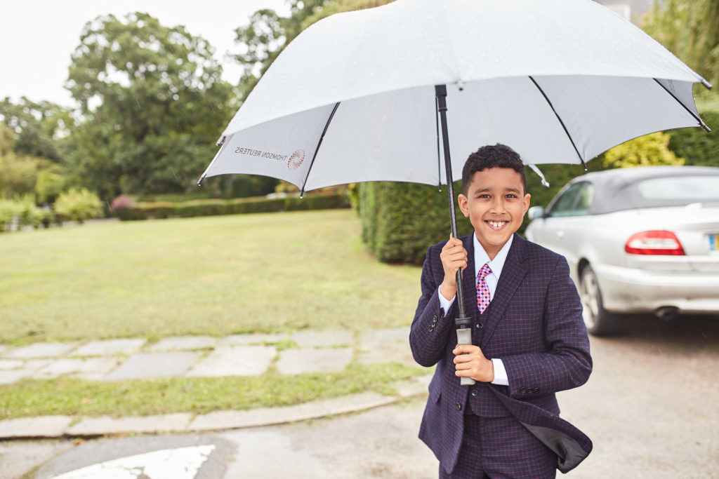 Young page boy in a suit holding a large umbrella