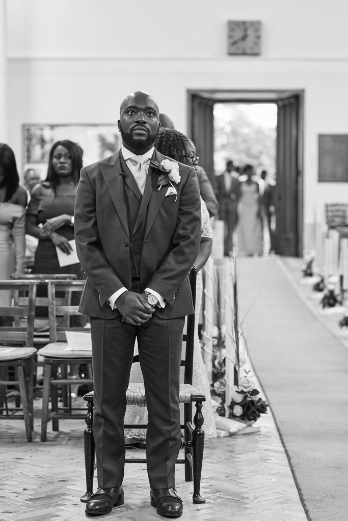Black and white photo of the groom waiting at the top of the aisle
