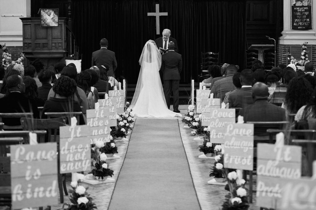 Black and white photo of the bride and groom at the altar, seen down the length of the aisle