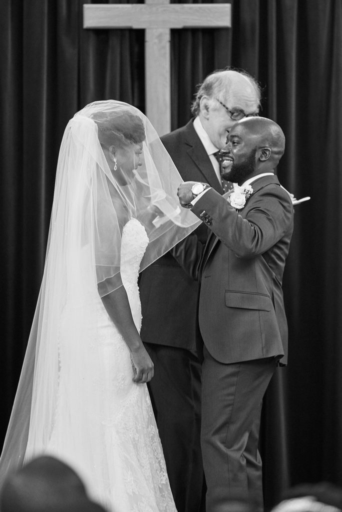 Black and white photo of the groom lifting the bride's veil