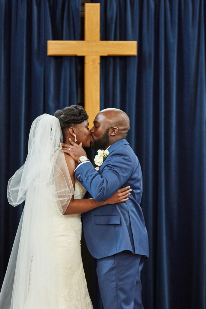 Bride and groom's first kiss beneath a wooden cross