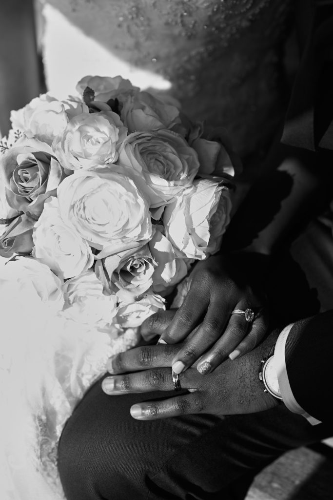 Black and white close-up of the bride's bouquet and the couple's hands showing their rings