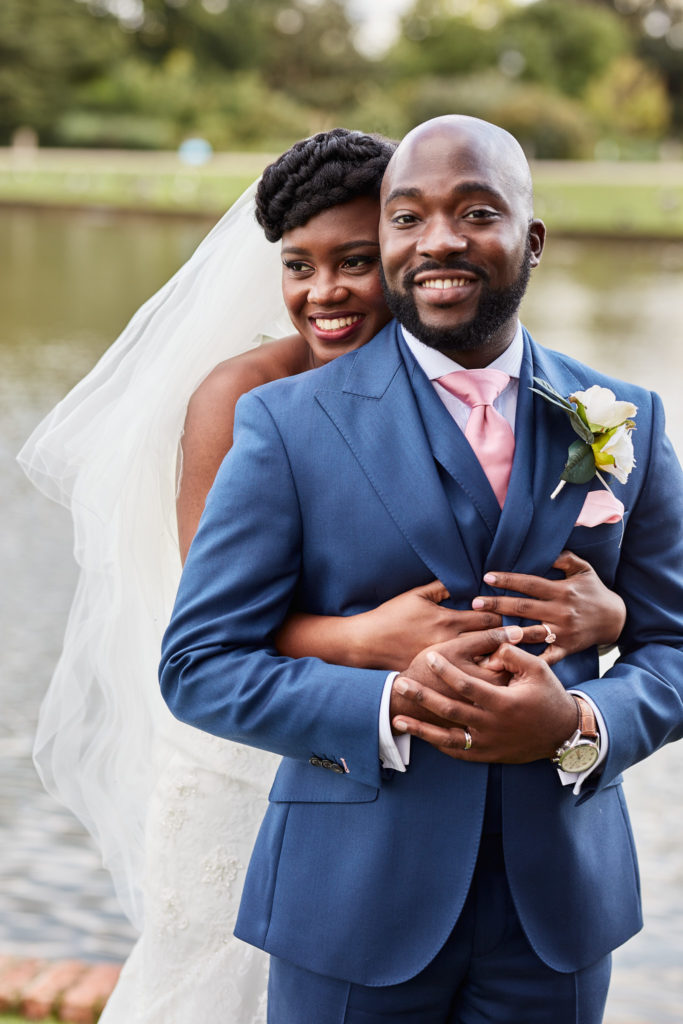 Bride hugging the smiling groom from behind beside the lake at Forty Hall