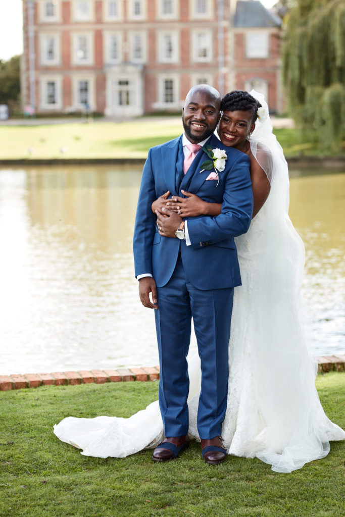 Bride hugging the groom from behind with Forty Hall across the lake