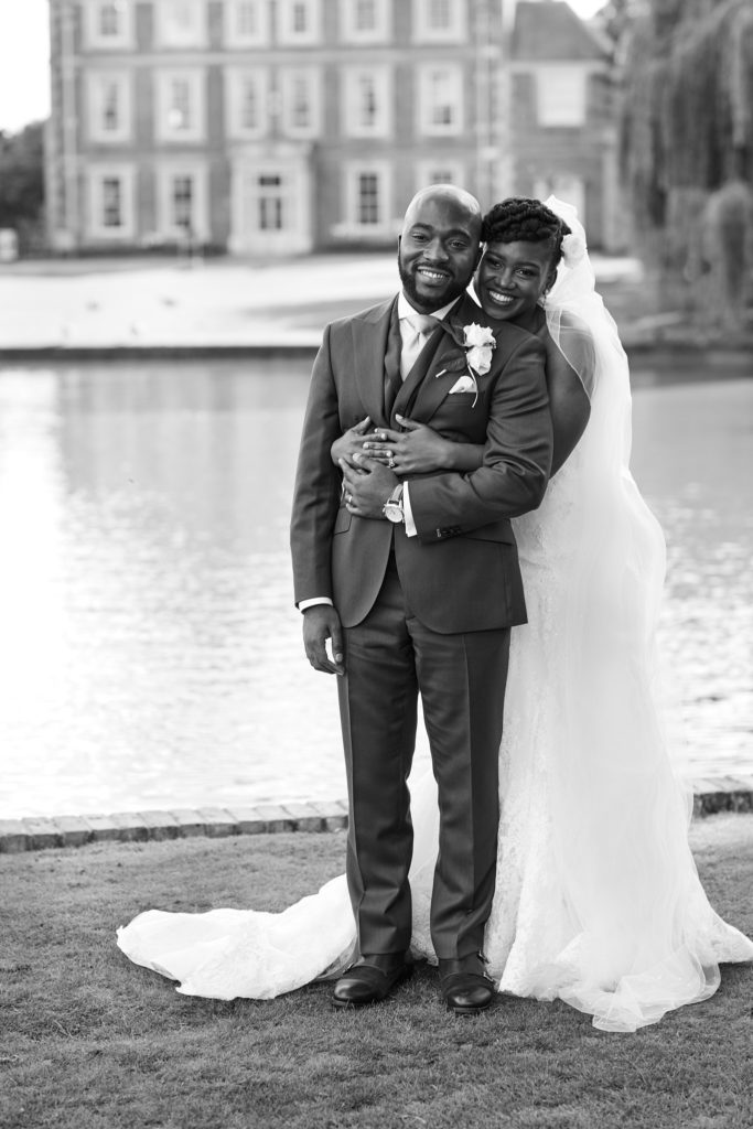 Black and white photo of the bride and groom with Forty Hall reflected in the lake behind them