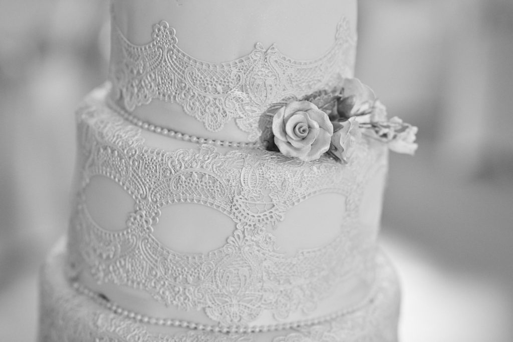 Black and white close-up of a lace-patterned wedding cake with a sugar rose
