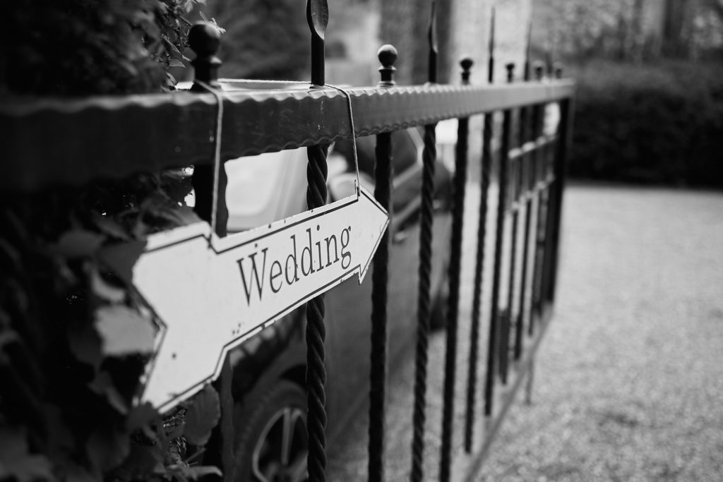 Black and white photo of a "Wedding" arrow sign on a gate