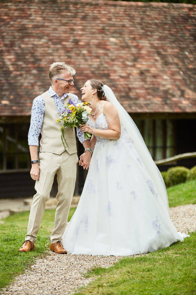 Bride and groom laughing on the path in front of the barn at the Lost Village of Dode