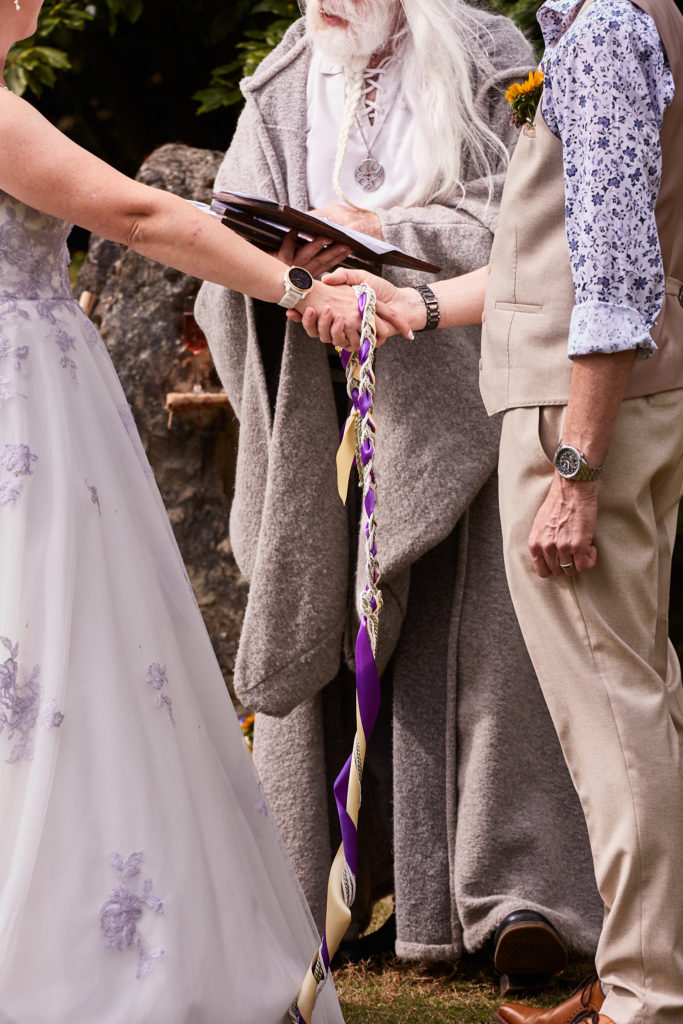 Close-up of the bride and groom's hands bound with ribbons during their handfasting